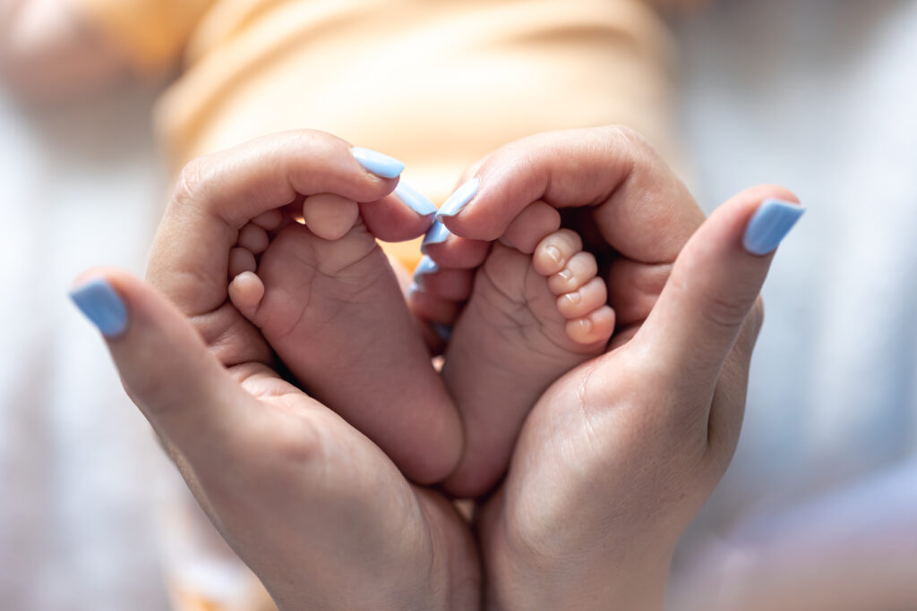 IVF Clinics in Dubai | A mother holds the legs of a newborn baby in her hands, in a close-up shot with soft focus, representing the concept of motherhood and care.